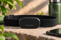 EKG-Brustgurt-Sensor auf einer Steinplatte. Aufschrift "EKG Sensor". Hintergrund Trinkflasche, Zimmerpflanze. Vordergrund Anschnitt Smartphone. AI Generated Label